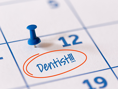 A pin on a calendar on the 12th of a month with dentist written in blue ink surrounded by a red circle.