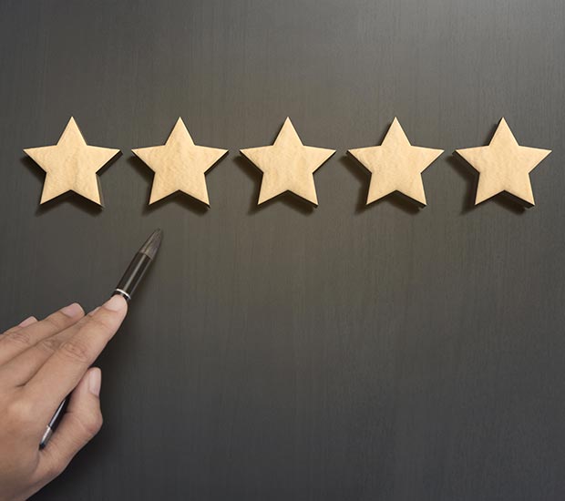 A person holds brown pen up to five gold stars hanging from a brown wall